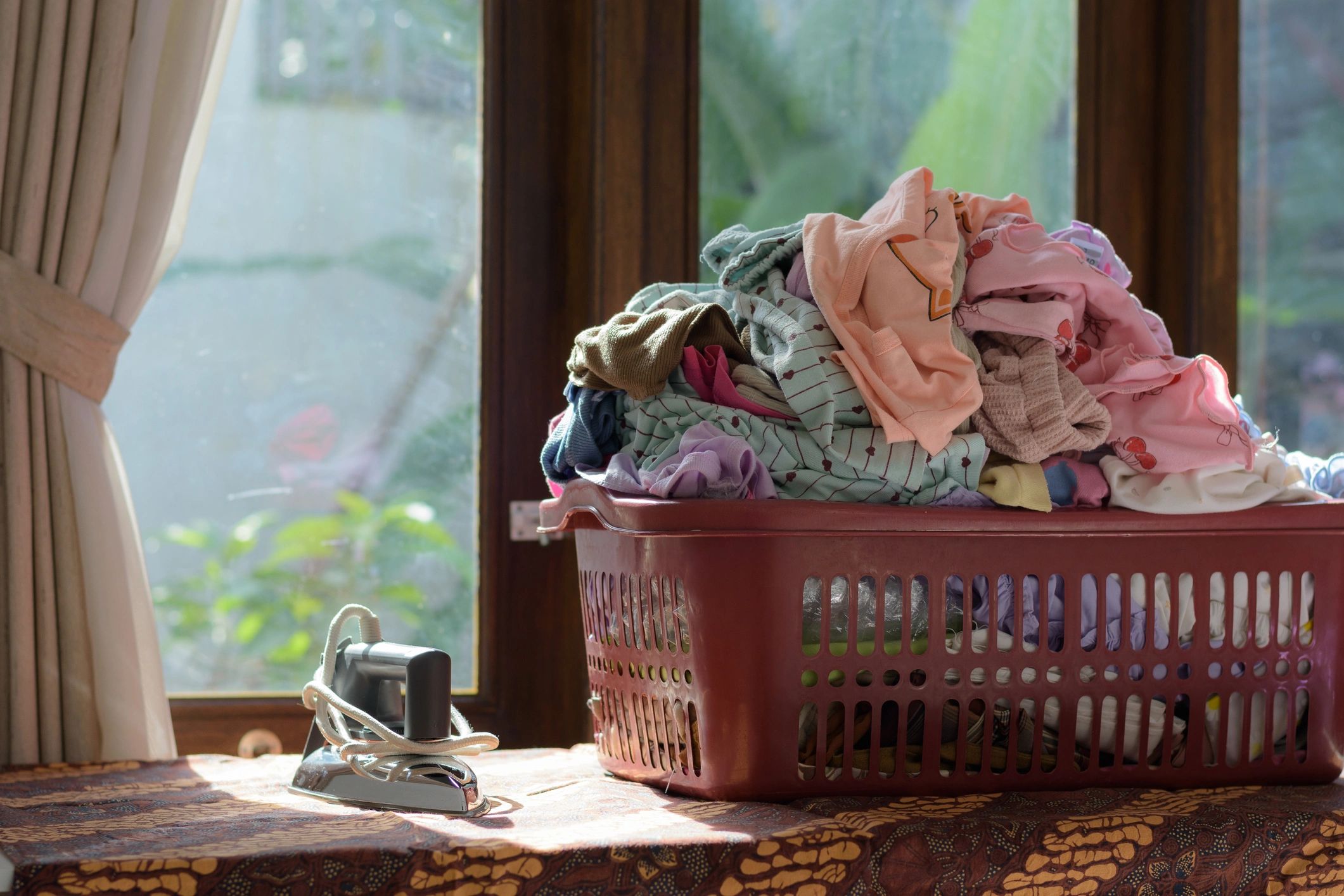 Laundry basket overflowing with clean clothes by a window